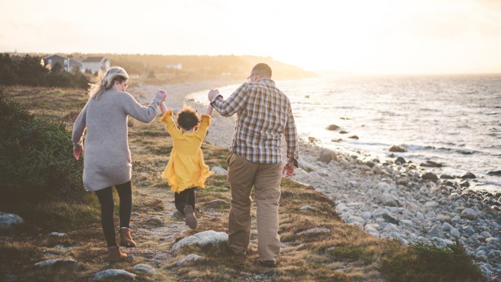Família a passear de mãos dadas junto ao mar ao pôr do sol