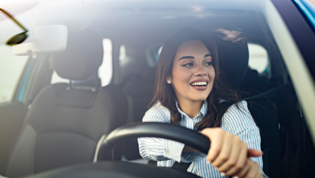 Condutor sorridente ao volante do carro, com a janela aberta